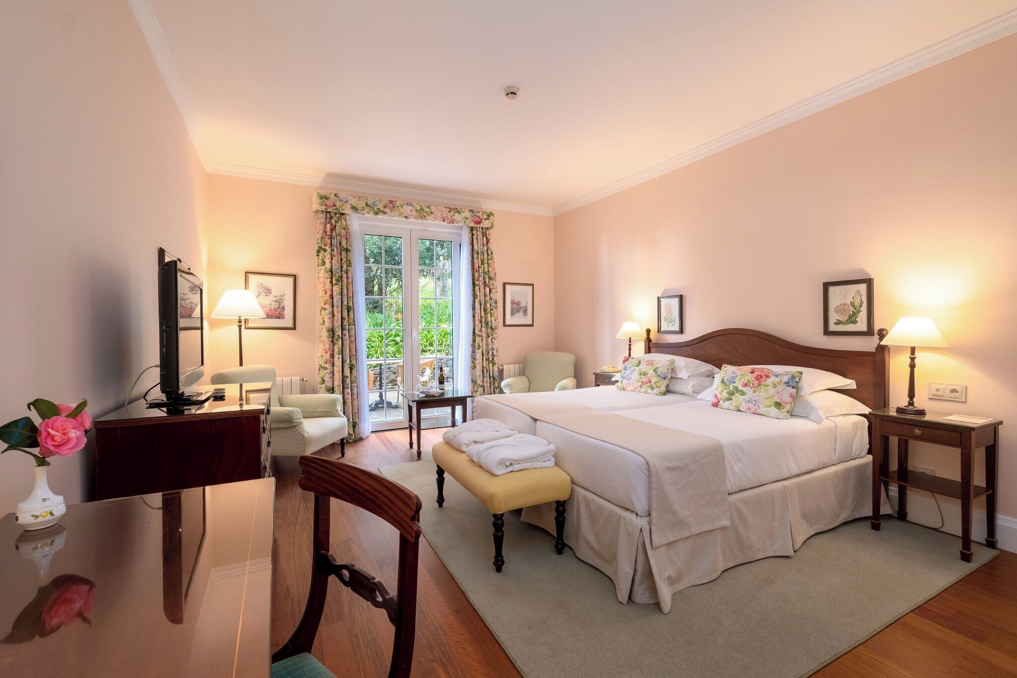 A bedroom with a large bed, bedside tables with lamps, a desk with a computer, and a chair.