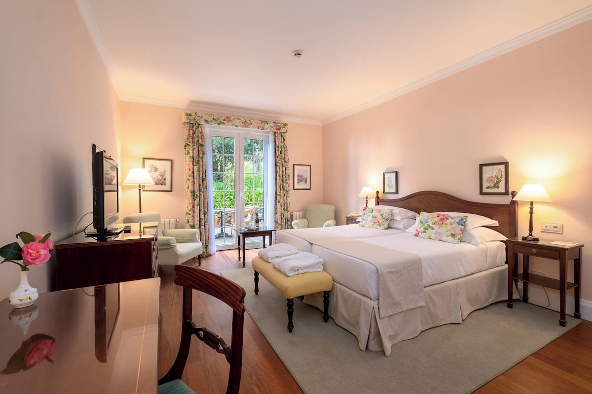 A bedroom with a large bed, bedside tables with lamps, a desk with a computer, and a chair.