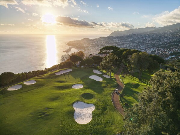 Ein Golfplatz mit Bunkern und einem Weg, der auf eine Küstenstadt mit Blick blickt.