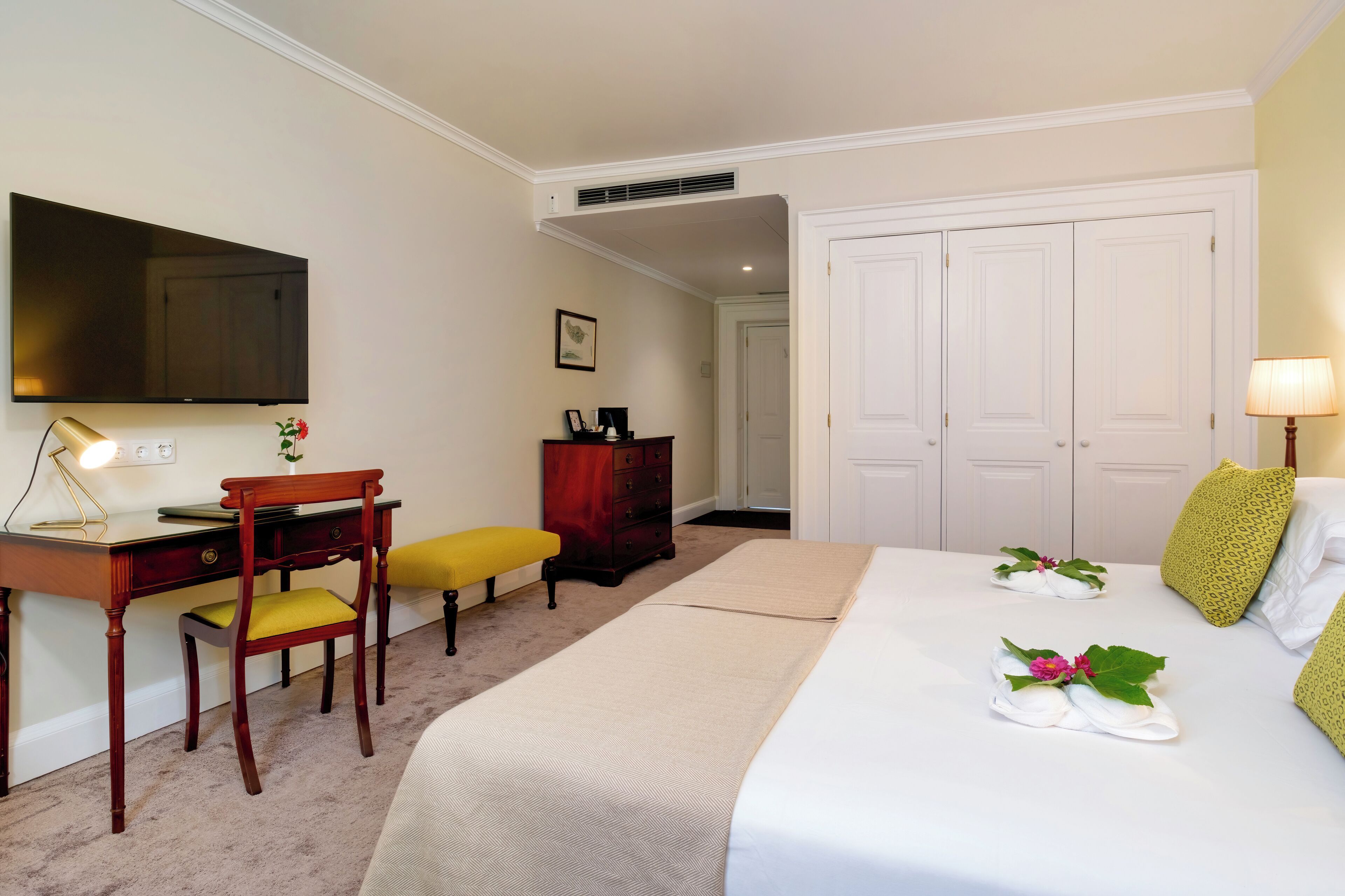 A hotel room with a bed, a desk, a chair, a TV, a wardrobe, and a lamp.