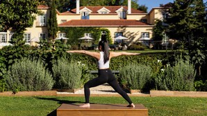 A person performing a yoga pose outdoors with a large building in the background. - Casa Velha do Palheiro, Relais & Chateaux (Funchal)