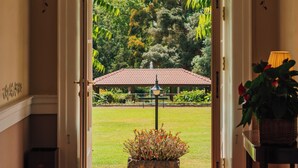 A doorway leading to a garden with a view of trees and a building in the background. - Casa Velha do Palheiro, Relais & Chateaux (Funchal)