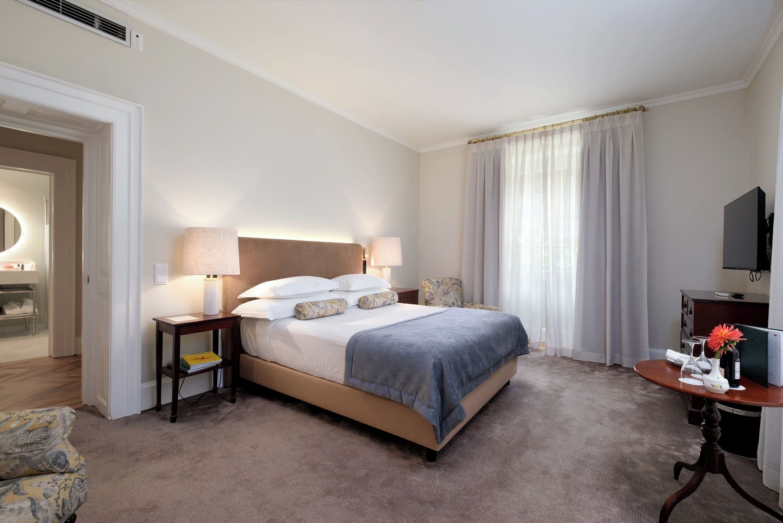 A hotel room with a large bed, bedside lamps, a desk with a vase, and a television.