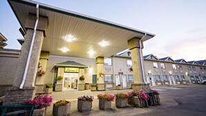 A hotel with a covered entrance, multiple windows, and flower planters in front. - Super 8 by Wyndham Drayton Valley (Drayton Valley)