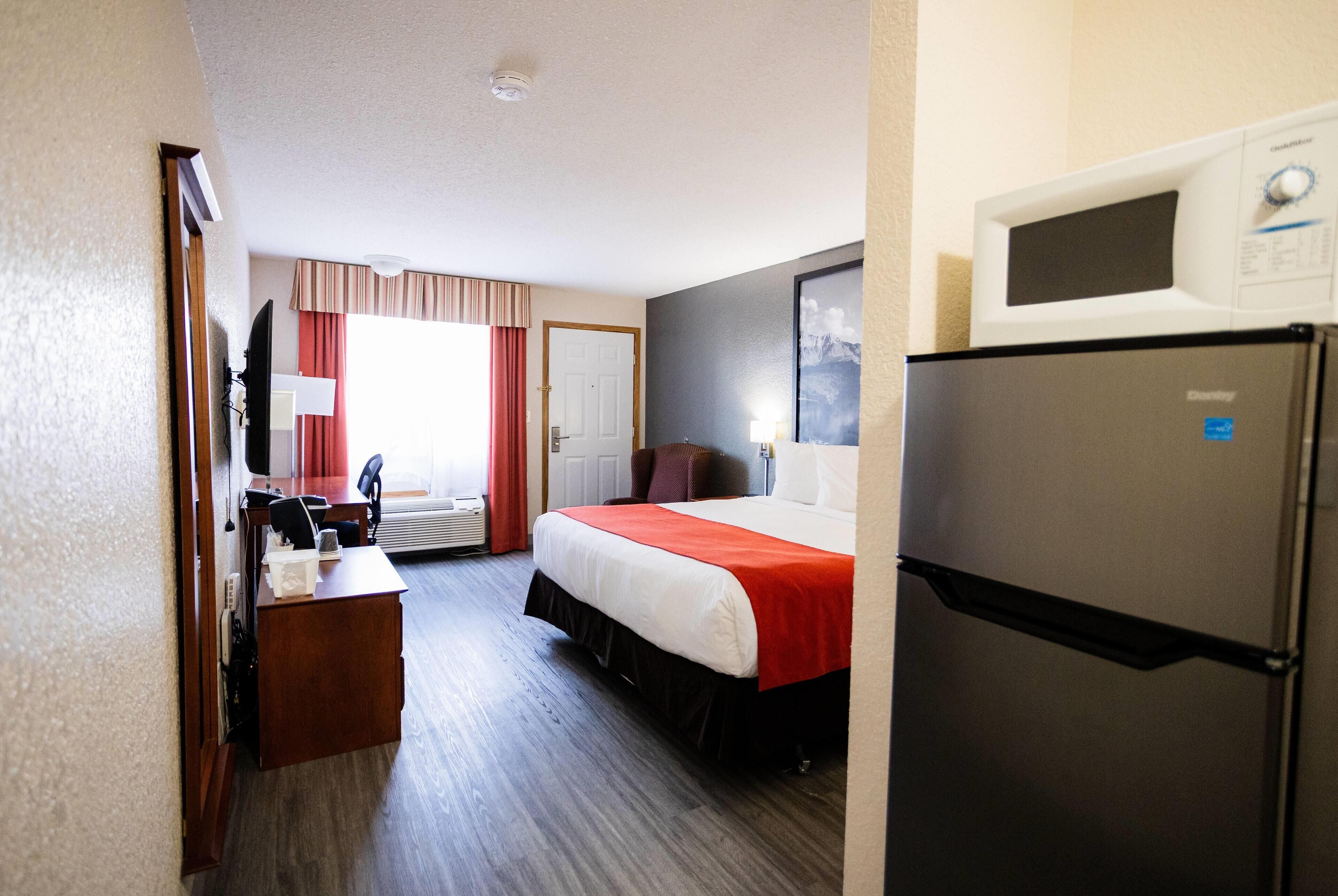 A hotel room with a bed, a desk, a chair, a television, a refrigerator, and a window with curtains.