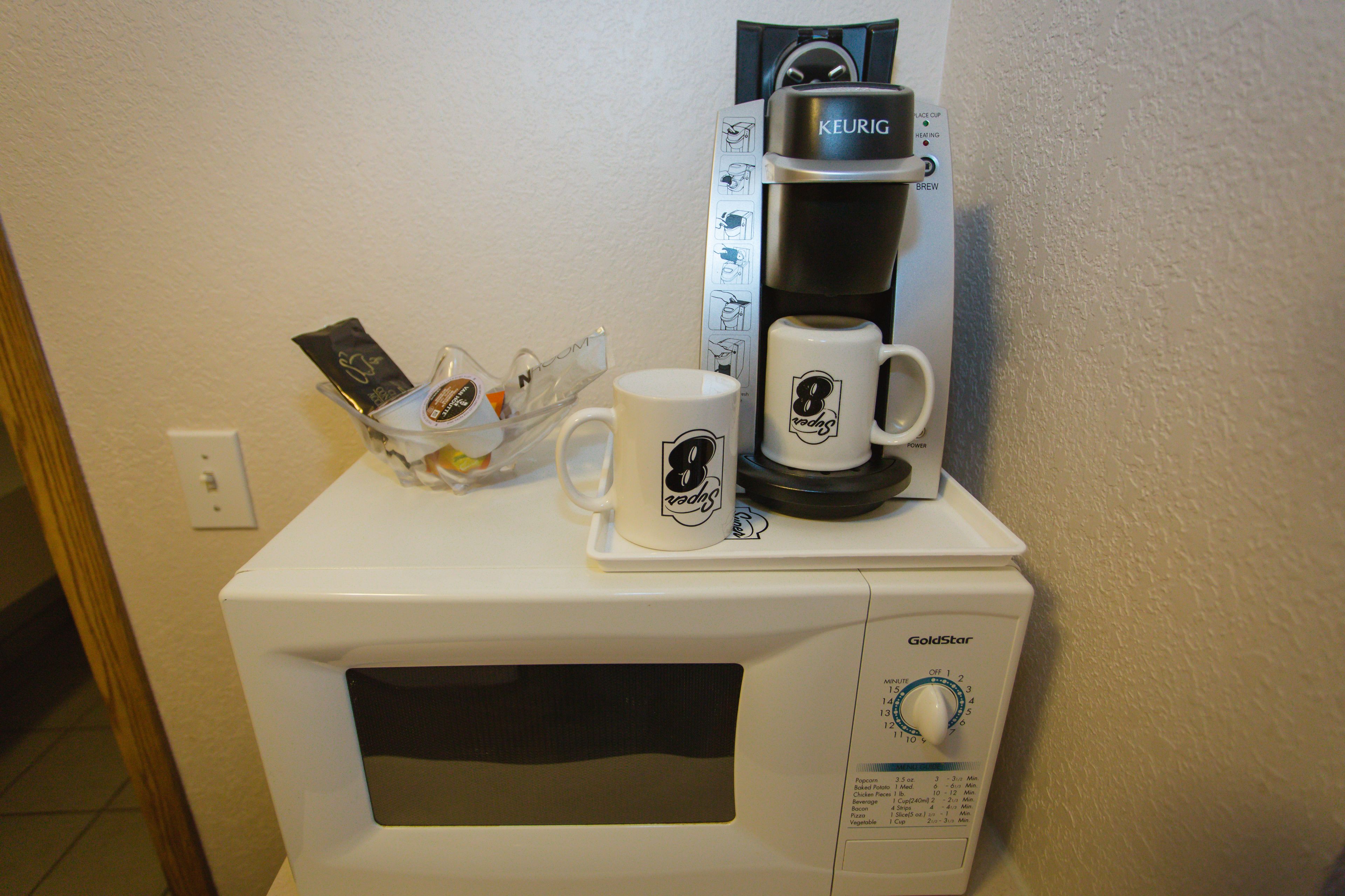 Un four à micro-ondes blanc, avec une machine à café et une tasse posée sur le dessus.