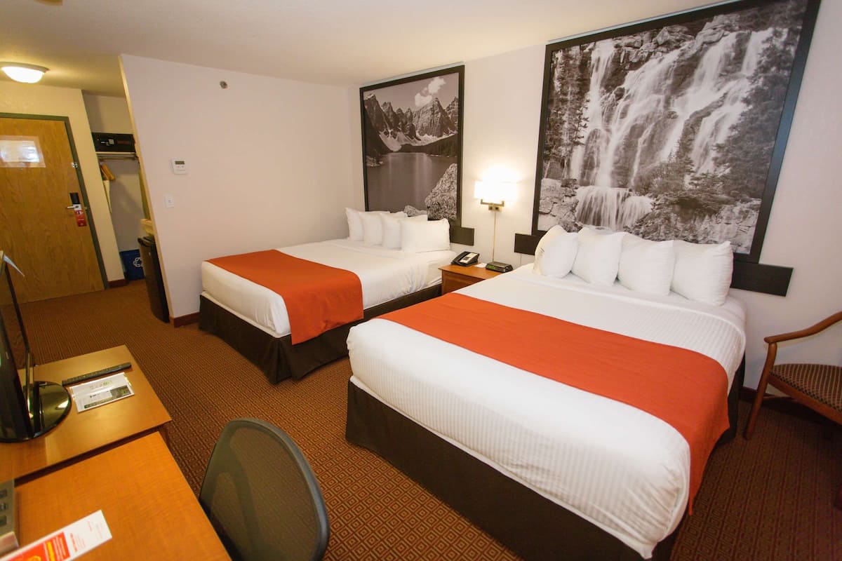 A hotel room with two beds, a desk with a chair, a telephone, and a wall-mounted lamp.