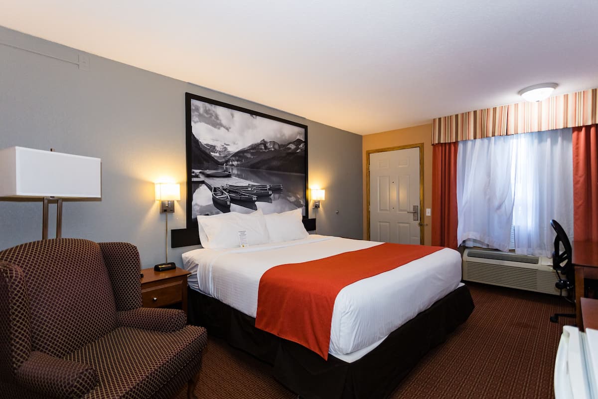 A hotel room with a large bed, a chair, a desk, and a wall-mounted TV.