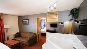A hotel room with a sofa, a small table, a bathtub, a TV, and a sign about jacuzzi tub rules. - Super 8 by Wyndham Drayton Valley (Drayton Valley)
