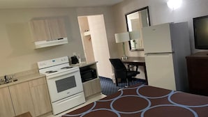 A compact hotel room with a kitchenette, a bed with a patterned bedspread, a desk with a chair, and a television. - Super 8 by Wyndham Red Deer (Red Deer)