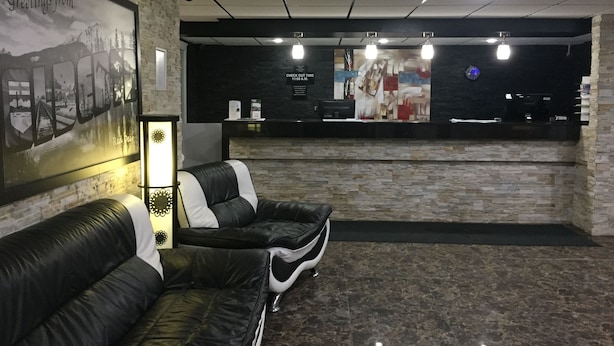 A reception area with a reception desk, a seating area with black leather sofas, a wall-mounted clock, and a framed picture of a mountainous landscape. - Super 8 by Wyndham Red Deer (Red Deer)