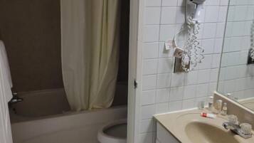 A bathroom with a toilet, a sink, a shower curtain, and a hairdryer mounted on the wall.