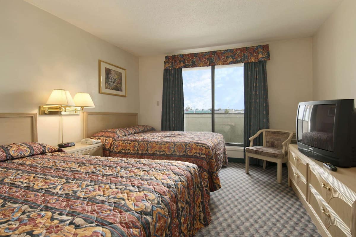A hotel room with two beds, a television, a chair, and a window with curtains.