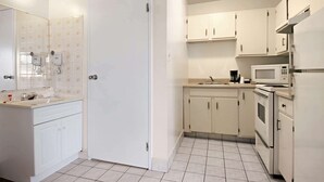 A compact kitchen with white cabinets, a microwave, and a stove. - Super 8 by Wyndham Red Deer (Red Deer)