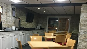 A restaurant with wooden tables and chairs, a stone wall, and a kitchen area. - Super 8 by Wyndham Red Deer (Red Deer)