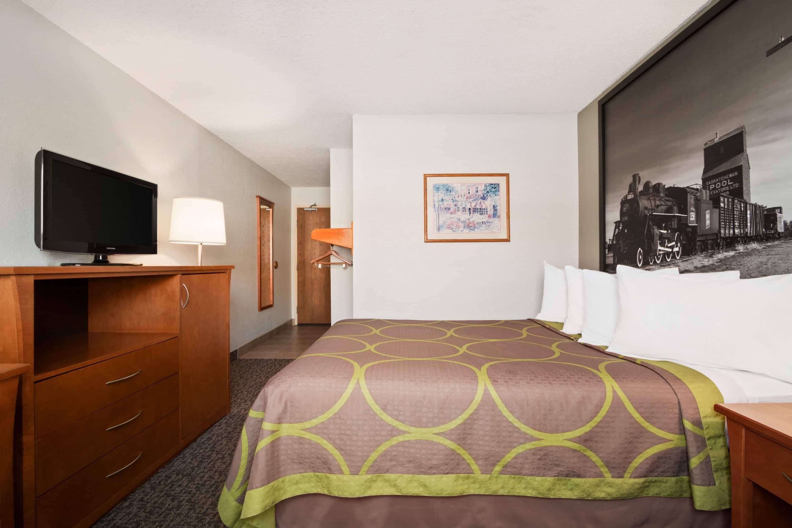 A hotel room with a bed, a television, a desk, and a framed picture on the wall.