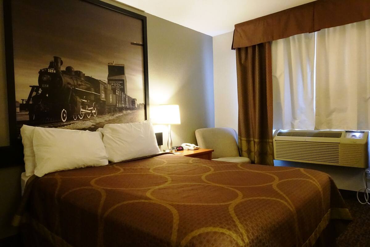 Une chambre d’hôtel avec un grand lit, une table de chevet, une lampe, une chaise et un appareil de climatisation.