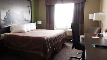 Una habitación de hotel con una cama grande, un escritorio, una silla, una lámpara y un ventanal con cortinas.