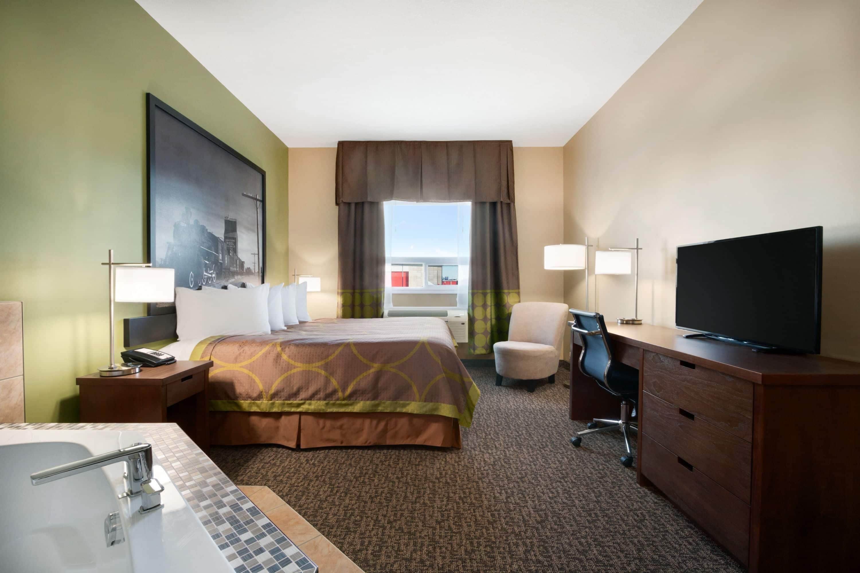 A hotel room with a bed, a desk with a chair, a television, a bathroom with a sink and mirror, and a large window with curtains.