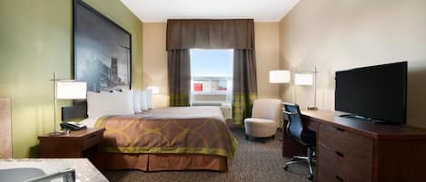 A hotel room with a bed, a desk with a chair, a television, a bathroom with a sink and mirror, and a large window with curtains.