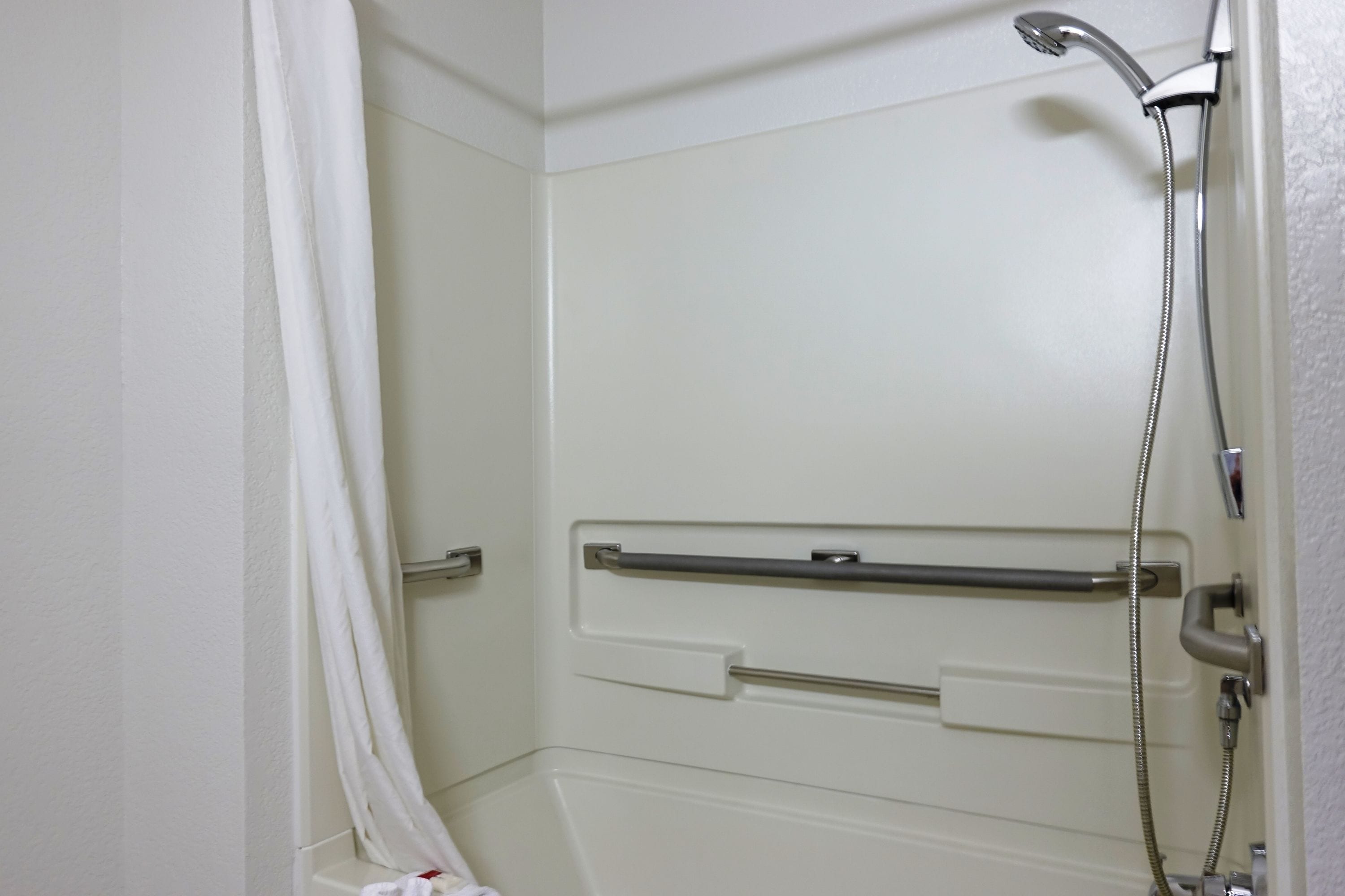 A bathroom with a shower, grab bars, and a white door.