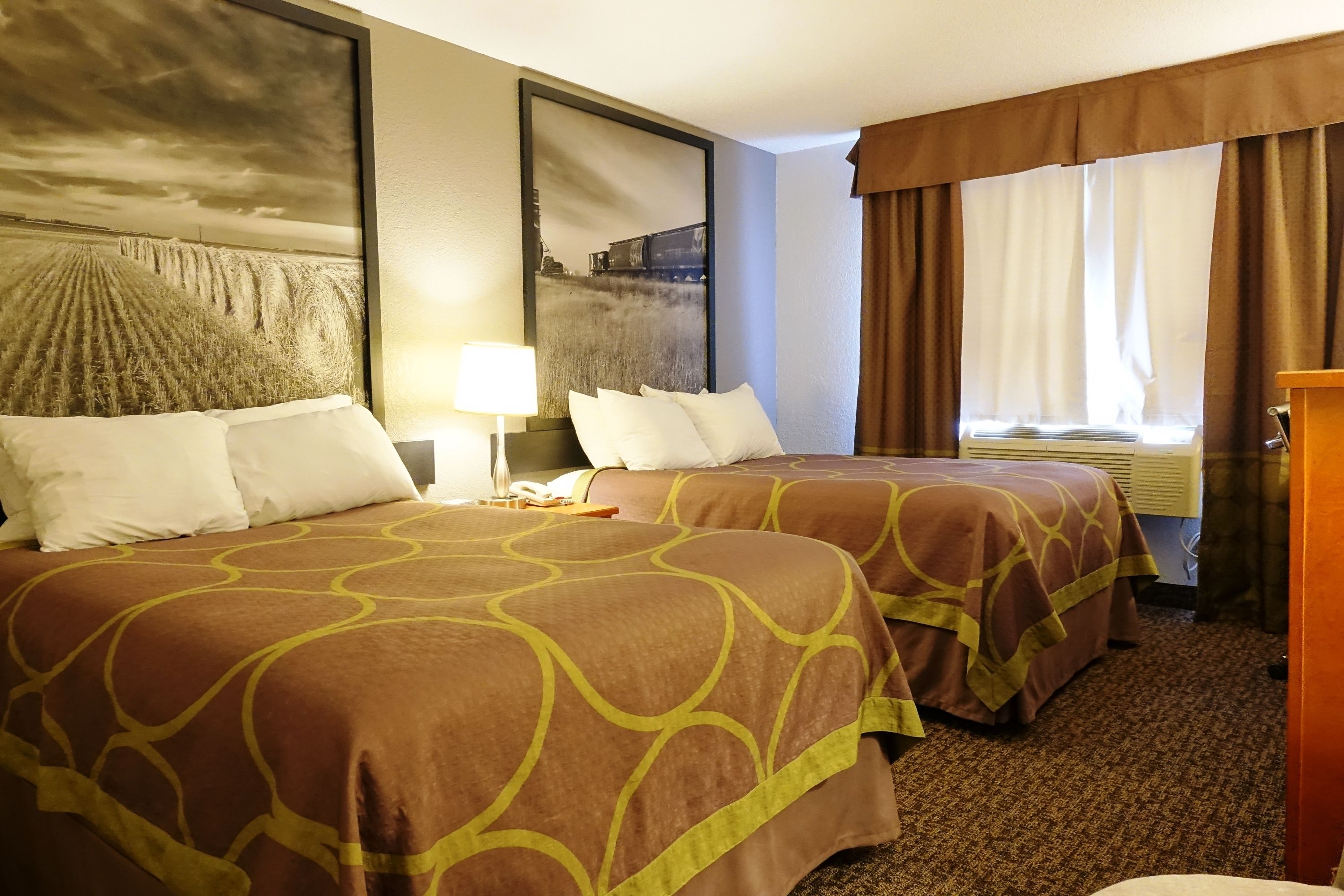 Habitación de hotel con dos camas, un cuadro grande en la pared, una ventana con cortinas y una mesita de noche con lámpara.