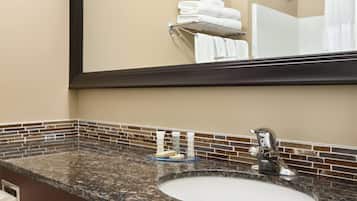 Baño con encimera de granito, lavamanos y espejo que refleja un perchero y la zona de la ducha.