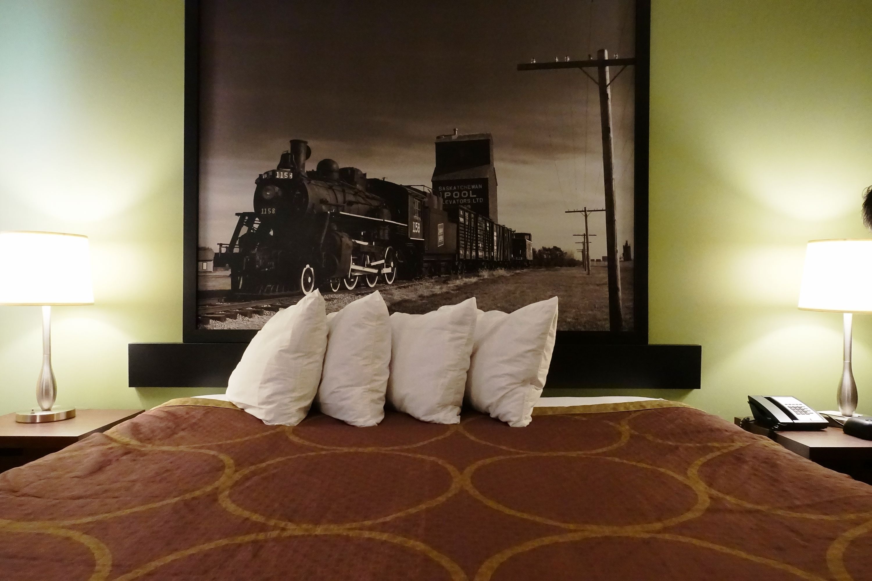 Una camera d'albergo con un letto, cuscini, una foto incorniciata di un treno appesa al muro e due abat-jour.
