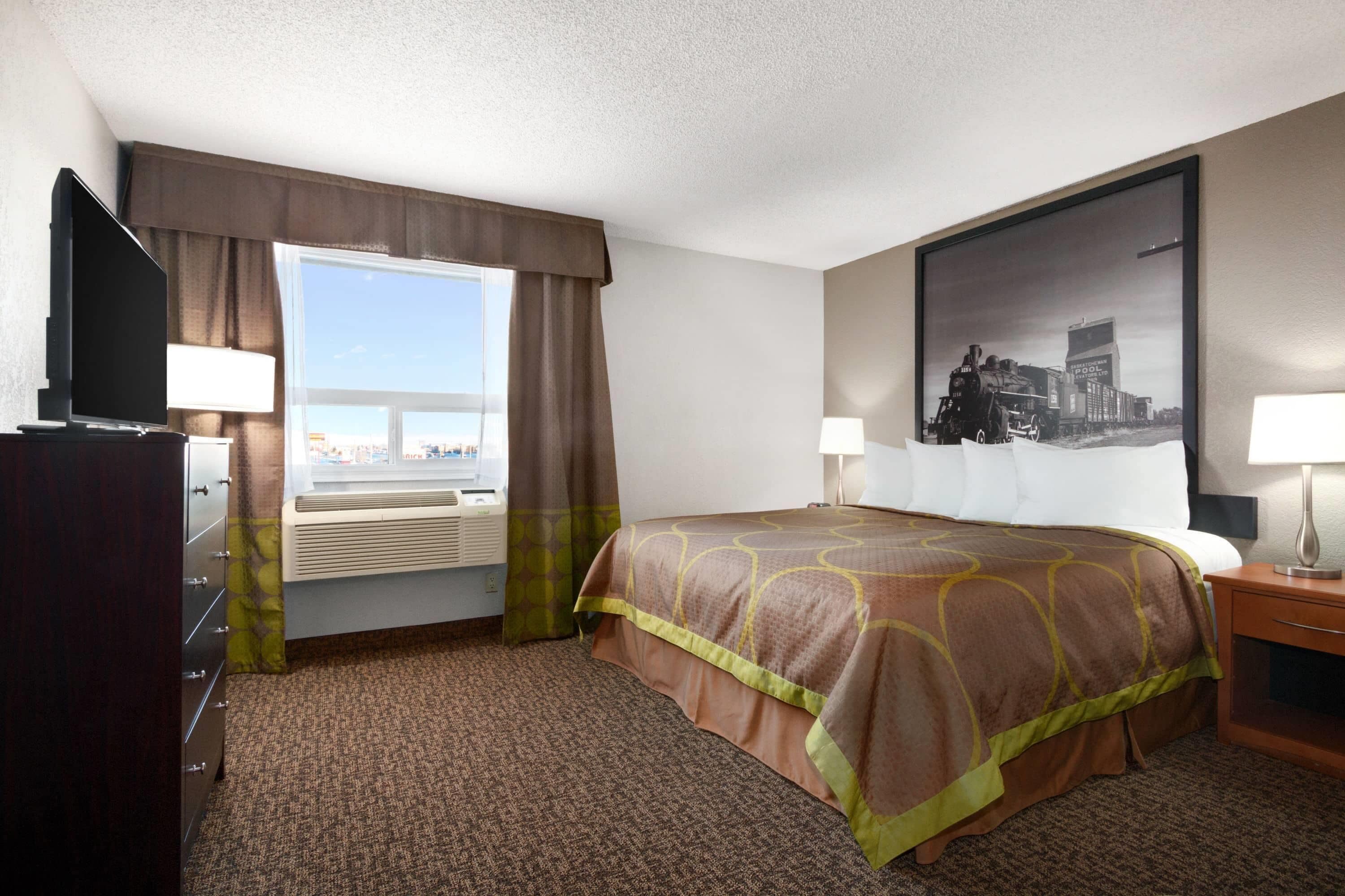 A hotel room with a bed, a desk, a television, a window with curtains, and a wall-mounted picture.