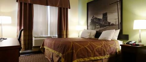 A hotel room with a bed, two bedside lamps, a desk, a chair, and a large framed picture on the wall.