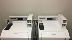 Deux lave-linge à chargement frontal blancs, dotés de panneaux de commande, d’un câble d’alimentation et d’un panneau de commande fixé au mur.