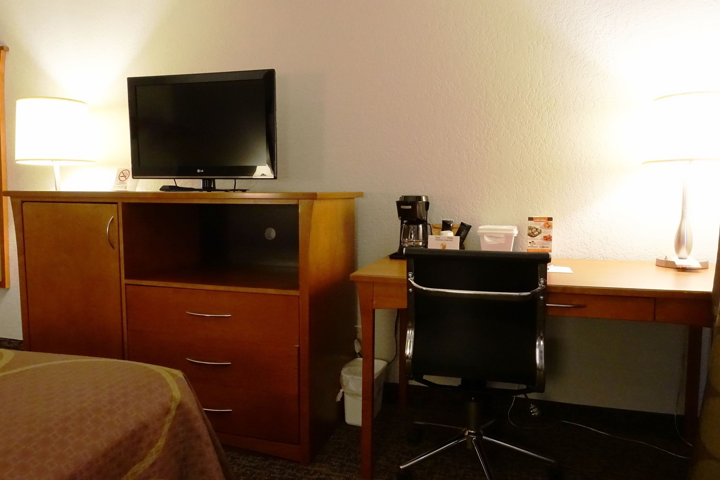 A hotel room with a bed, a desk with a chair, a television, and a coffee maker.
