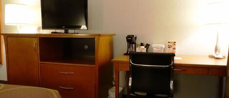 Una habitación de hotel con cama, escritorio con silla, televisor y cafetera.