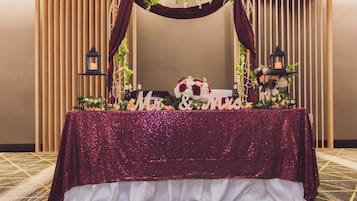 Una mesa con un mantel brillante, un arreglo floral y dos faroles.