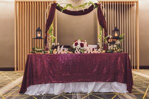 A table with a sparkly tablecloth, a floral arrangement, and two lanterns. - Holiday Inn Fredericksburg Conference Ctr by IHG (Fredericksburg)