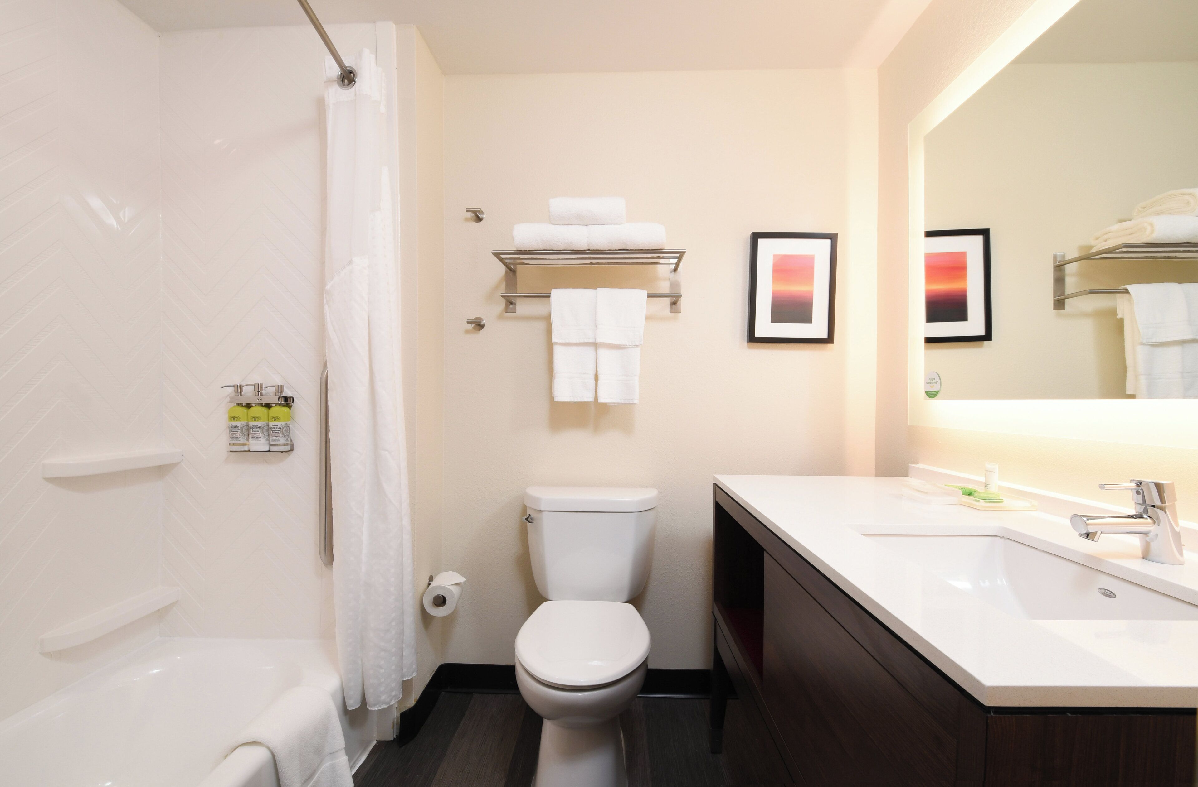 Un baño moderno con bañera, inodoro y lavamanos. Se observan toallas y un rollo de papel higiénico.
