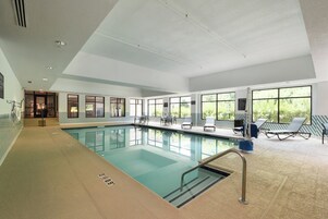 Une piscine intérieure à l’eau claire, entourée de chaises longues et dotée de grandes fenêtres.