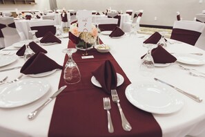 Une table dressée pour un événement formel, avec de l’argenterie, des assiettes blanches et un chemin de table rouge.