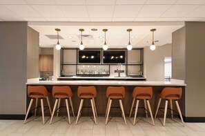 A bar area with a long counter, multiple stools, and overhead lighting. - Holiday Inn Fredericksburg Conference Ctr by IHG (Fredericksburg)