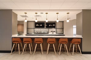 Una zona de bar con una barra alargada, varios taburetes e iluminación colgante.