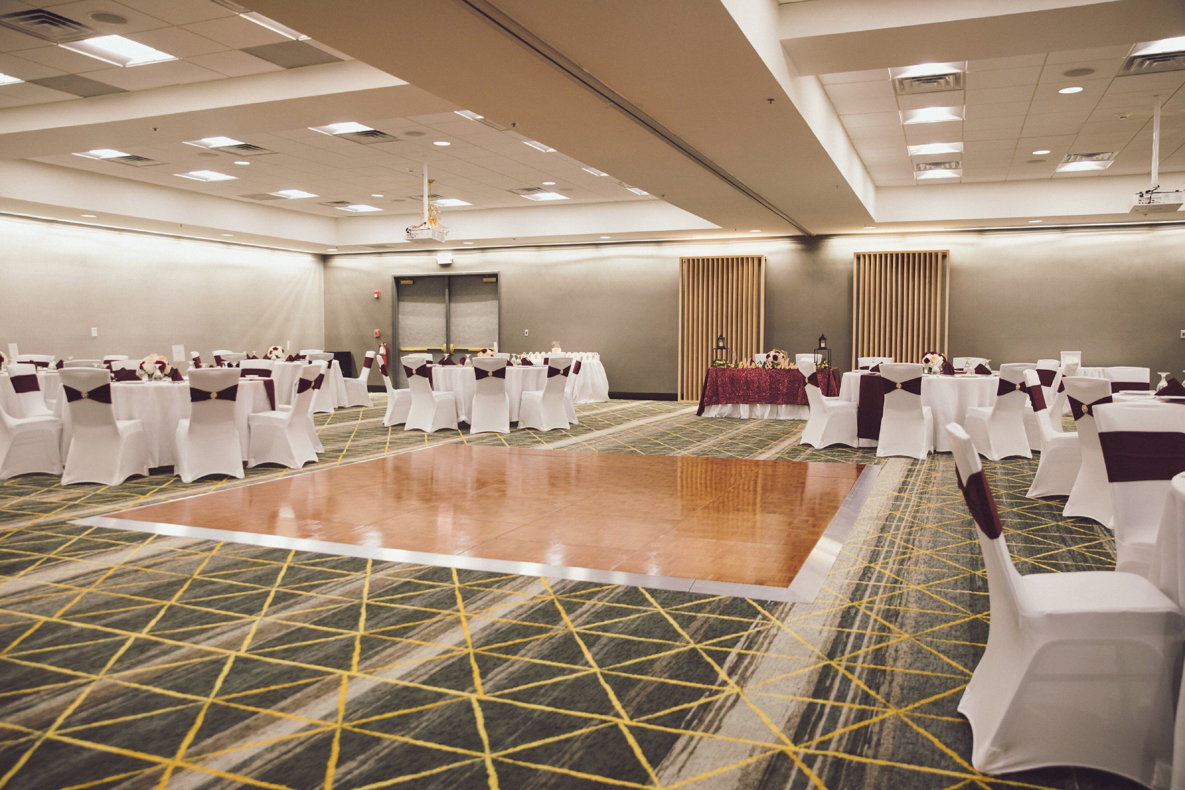 A conference room with a large dance floor, rows of tables with chairs, and a carpeted floor.