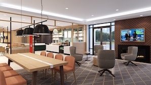 A modern interior with a dining area, seating, a fireplace, and a TV screen. - Holiday Inn Fredericksburg Conference Ctr by IHG (Fredericksburg)