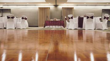 Un salón de conferencias con piso de madera pulida, sillas blancas con cintas oscuras y una mesa con mantel rojo.