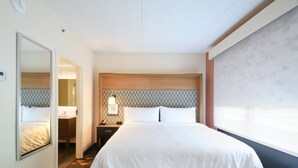 Une chambre d’hôtel avec un grand lit, une table de chevet avec une lampe, un miroir et une vue sur l’extérieur par une fenêtre.