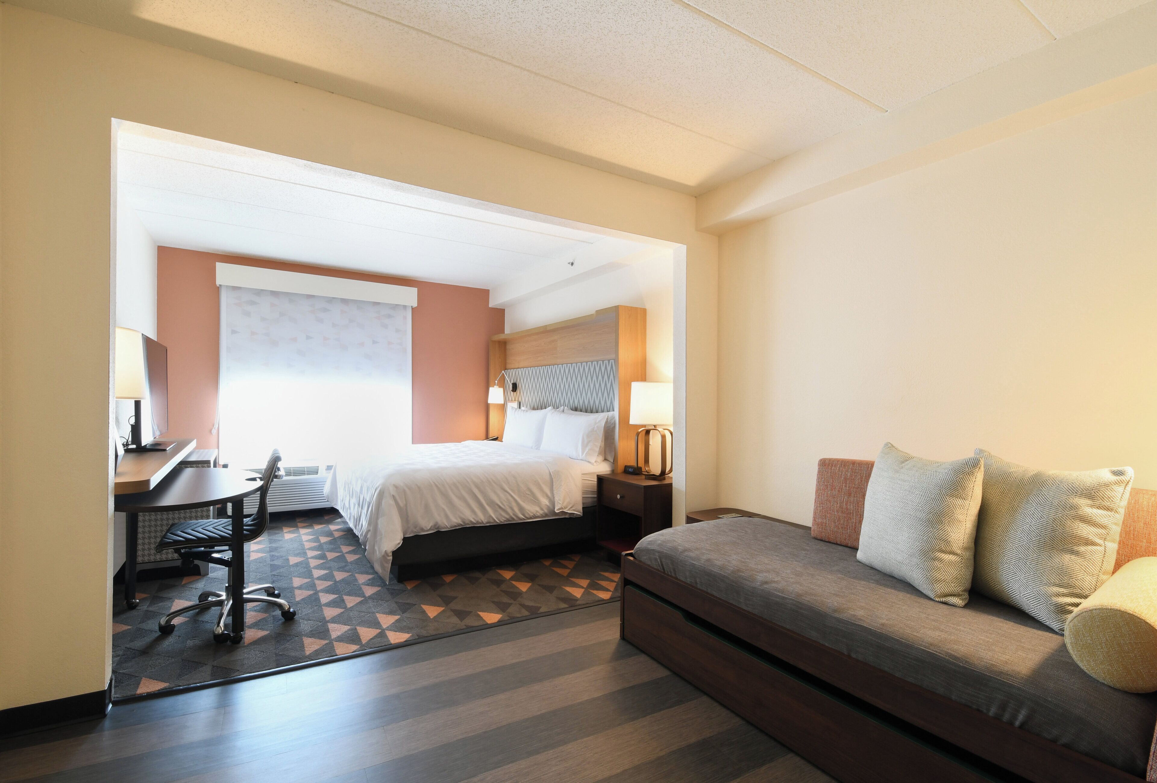 Een hotelkamer met een bed, een bureau met stoel, een bank en een kamerkleed met dessin.