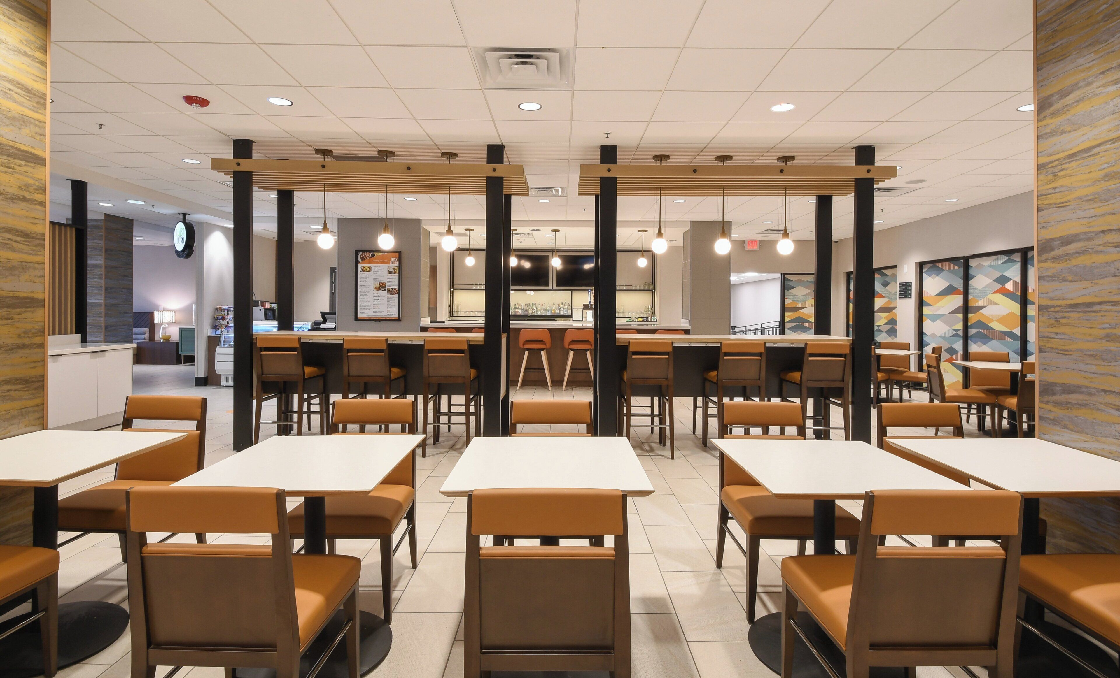 Un interior de restaurante moderno con varias mesas, cabinas, una barra y una pantalla con el menú.