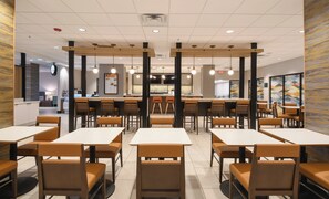 Un interior de restaurante moderno con varias mesas, cabinas, una barra y una pantalla con el menú.