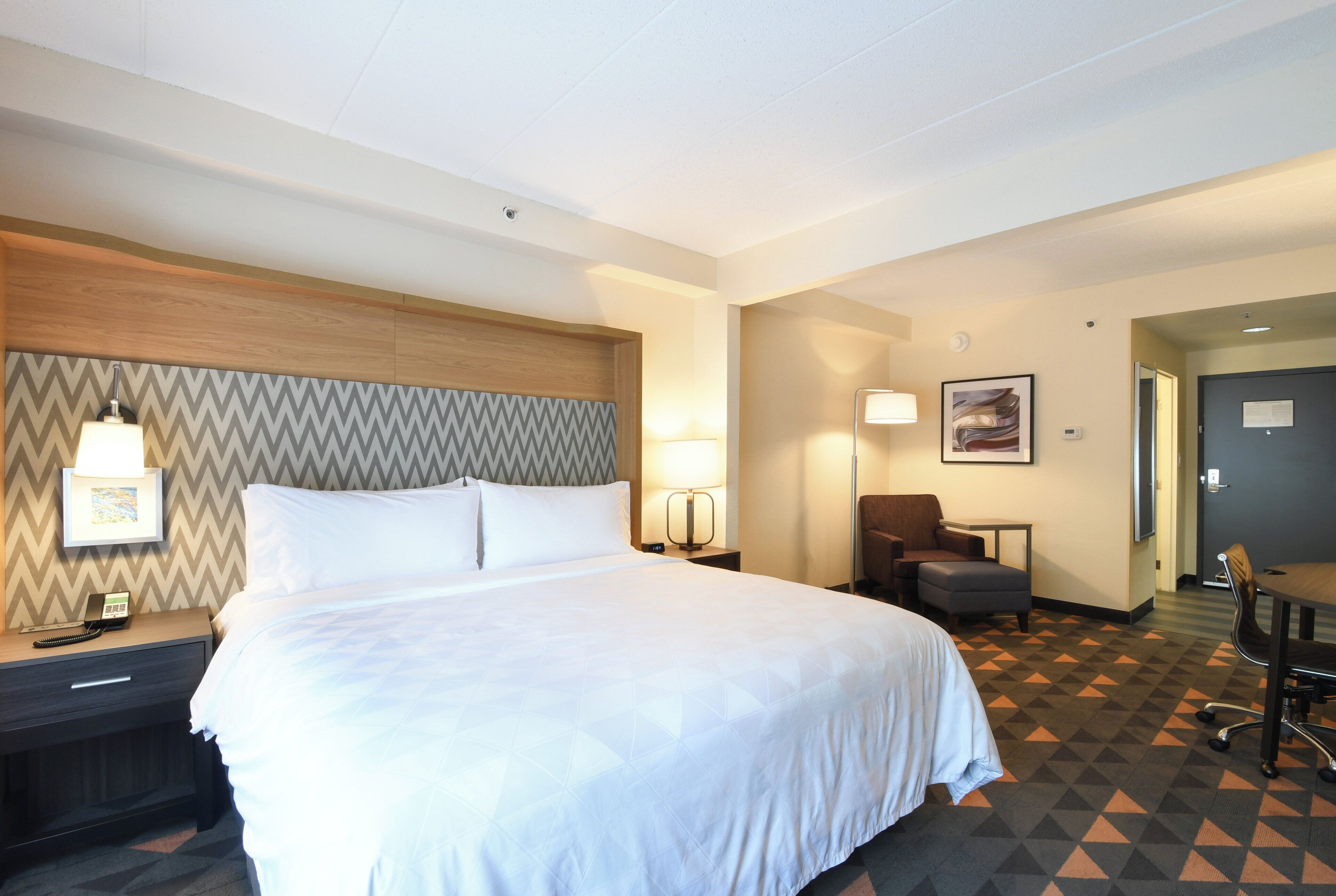 A hotel room with a large bed, a desk with a telephone, a chair, and a small table.