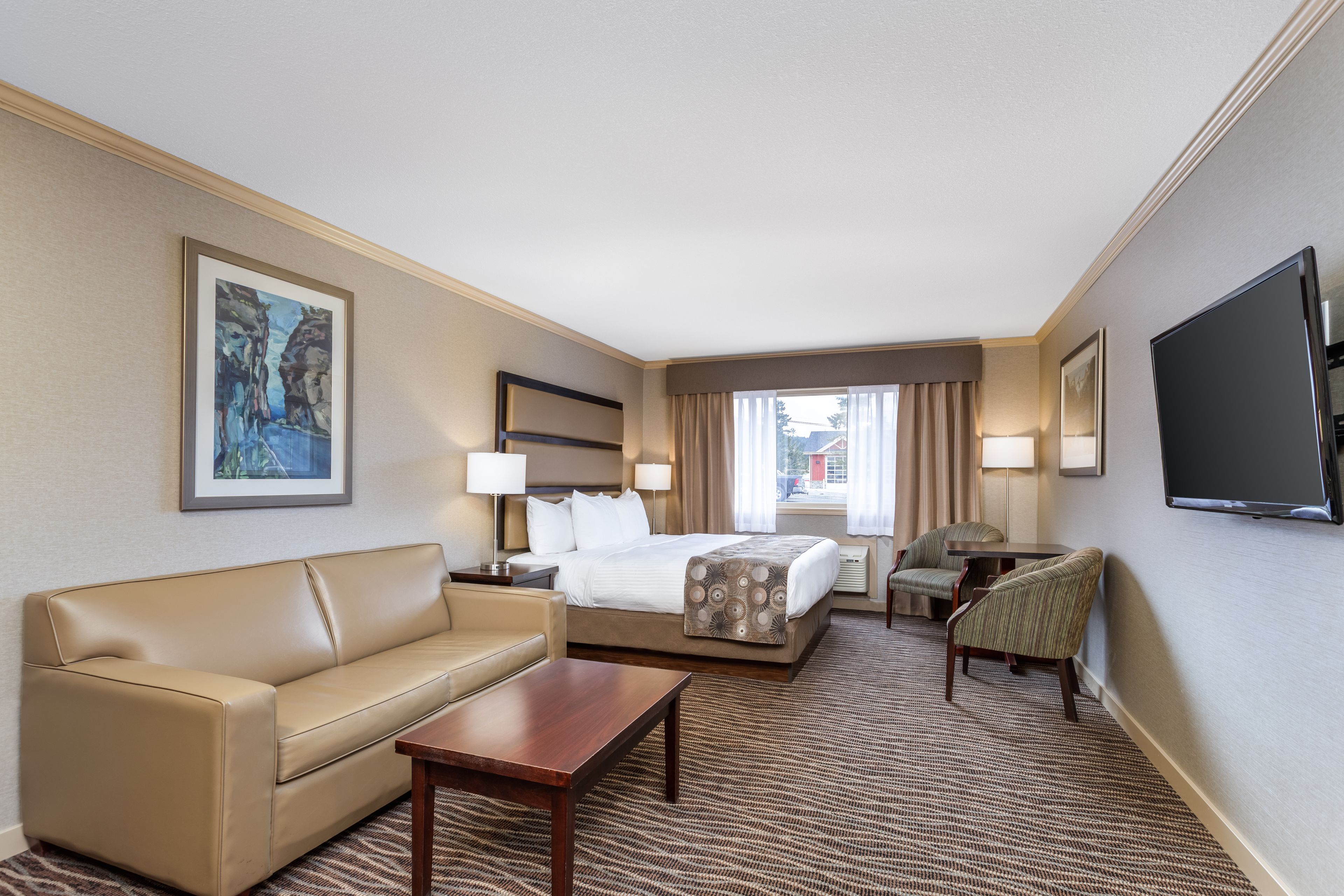 A hotel room with a bed, a sofa, a chair, a TV, and a painting on the wall.