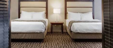 A hotel room with two beds, a patterned carpet, a nightstand with a lamp, and a ceiling light.